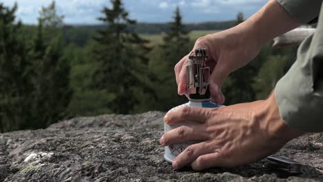 man preparing outdoor gas stove on rocky hill, camp gas stove forest close up