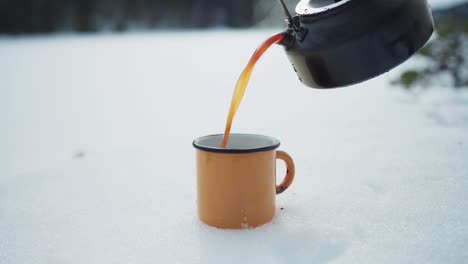 person pouring hot tea from kettle to a vintage cup in winter outdoor