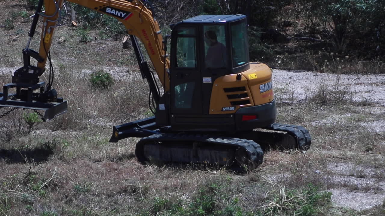 disparo en cámara lenta en un día ventoso pero soleado de una excavadora de maquinaria de planta conduciendo a través de la tierra semiseca después de cortar y casar arbustos