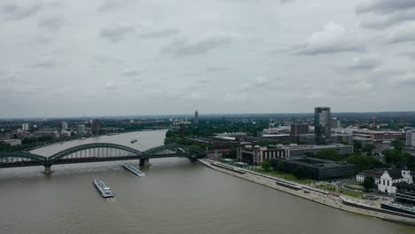 Aerial-shot-of-drone-flying-above-the-Rhine-river-in-city-of-Cologne-with-bridge-and-traffic-in-the-background