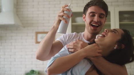una joven pareja casada jugando con crema batida en casa.