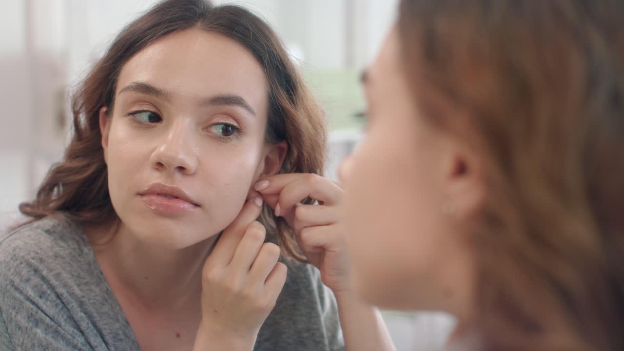 mujer alegre poniendo pendientes a la oreja mirando en el espejo del baño en casa