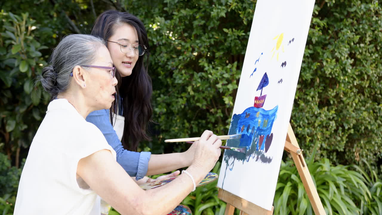 Painting on canvas, asian grandmother and granddaughter creating outdoor artwork together