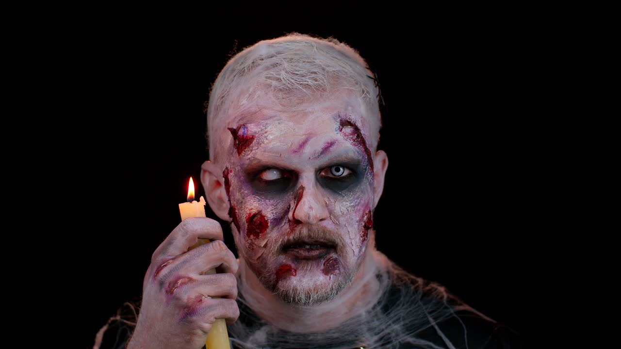 Uomo con trucco zombie di Halloween, insanguinato e ferito, che cerca di spaventare, pronuncia incantesimi o evoca spiriti sopra una candela.