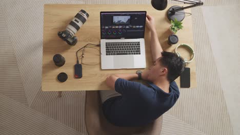 top view of asian male color grading sleeping while sitting in the workspace using a laptop next to the camera editing the video at home