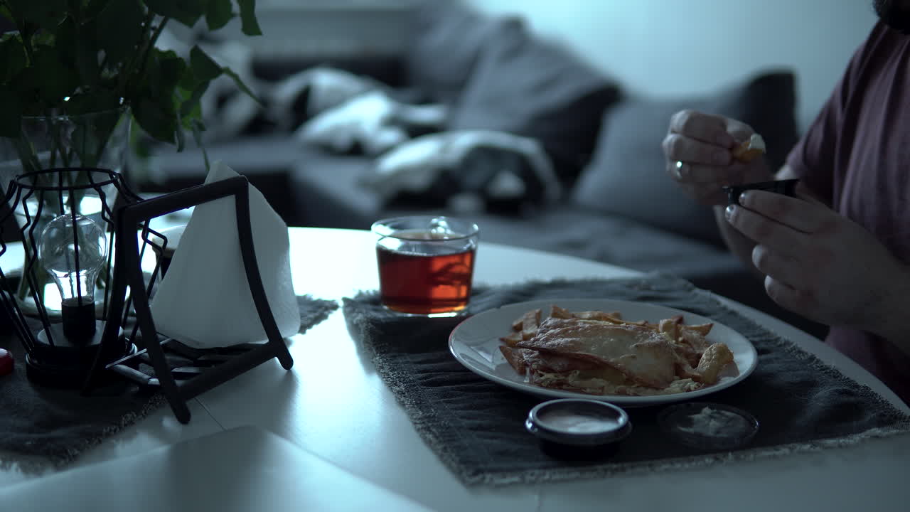 Open the sauce container and soak the chips in the sauce, man sitting on white table at home