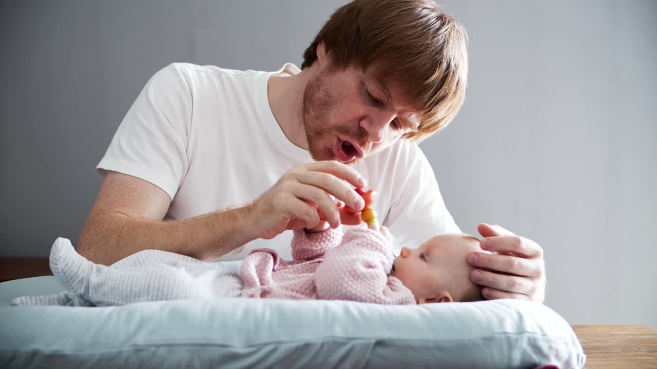 Playful dad and baby daughter playing with rattle toy or soother