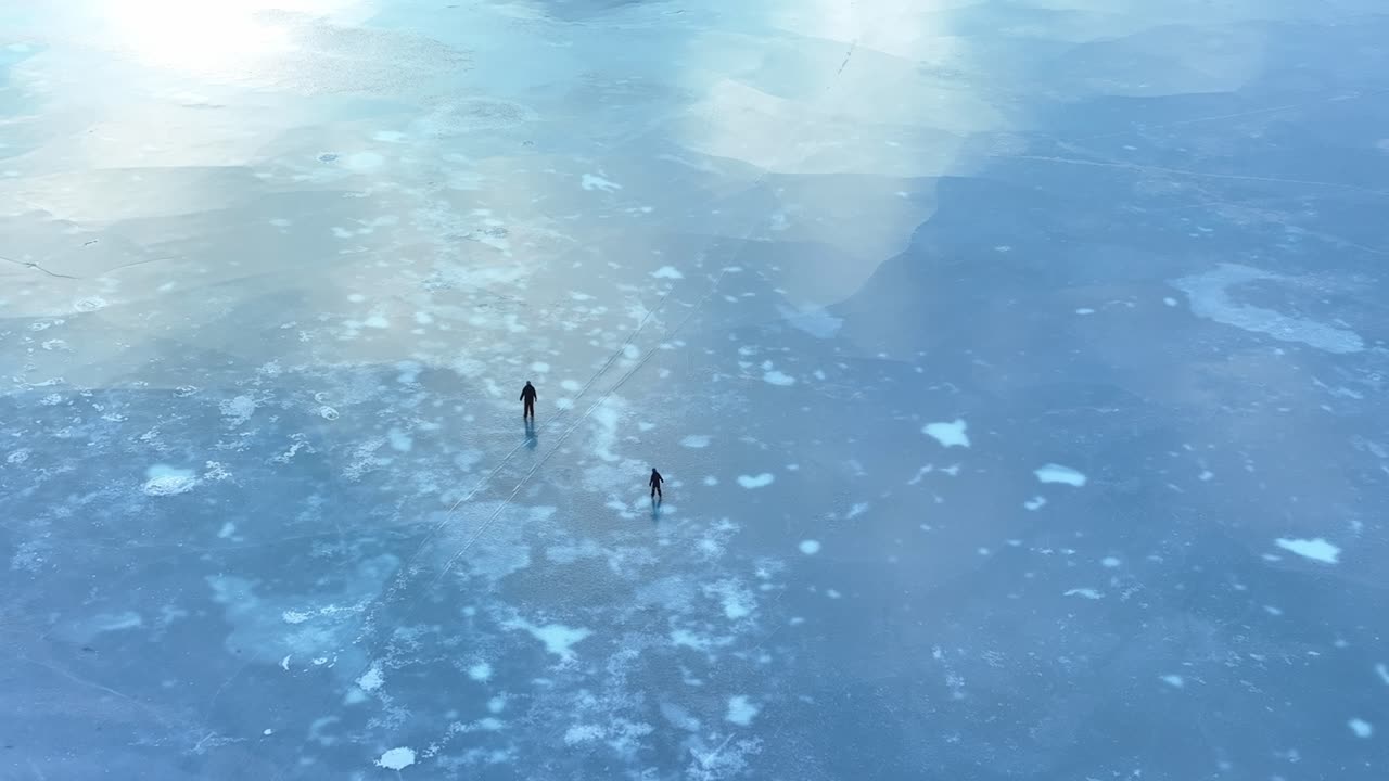 Static aerial view of father and daughter skating on frozen lake in calm winter light