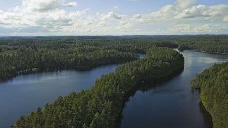 Aerial-footage-of-a-Finnish-lake-in-summer,-blue-sky,-heavy-clouds-and-sun,-long-island