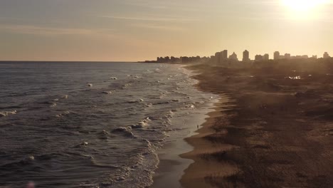 aerial panorama: waves of atlantic ocean reaching playa brava in uruguay during golden sunset - punta del este city in background