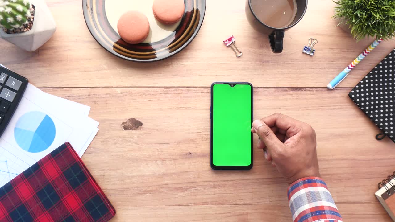 persona usando un teléfono inteligente con pantalla verde en un escritorio de madera