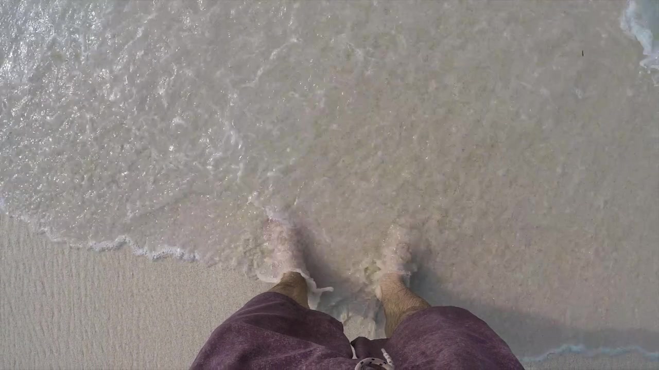 Splendida inquadratura di onde che si infrangono su piedi saldamente piantati su una spiaggia a Bali, Indonesia