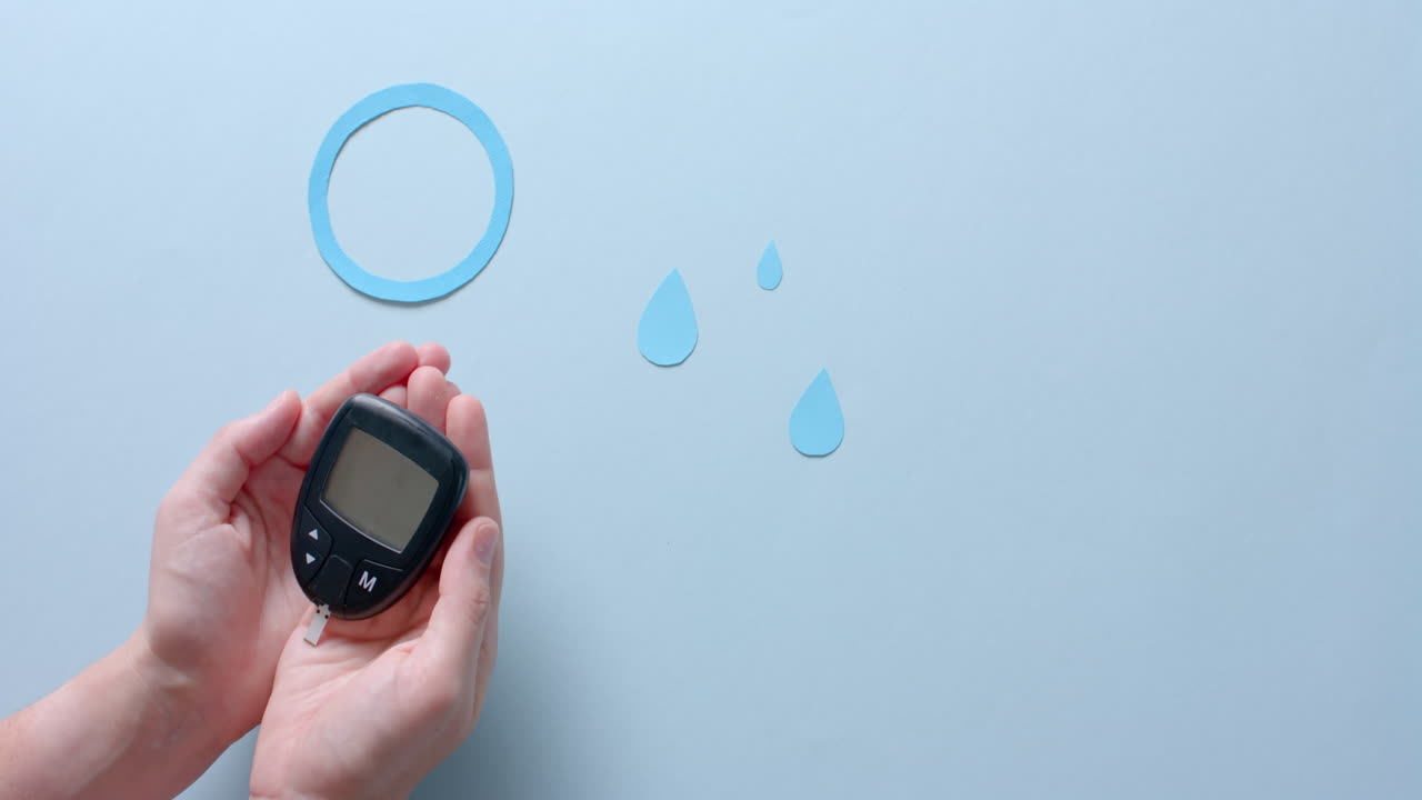 Hands of caucasian woman holding glucometer over blue drops and circle on pale blue, slow motion