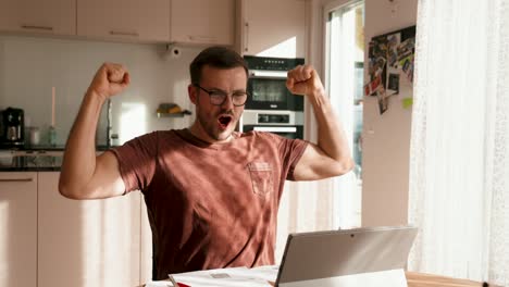 a young man at his laptop is very happy and shows happy emotions in slow motion. sunny day at home