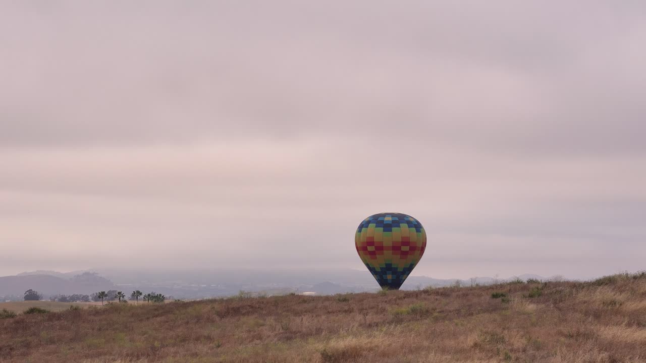 Festival dei Palloni Aerostatici e del Vino di Temecula, vista drone di un pallone colorato in fase di atterraggio dietro una collina