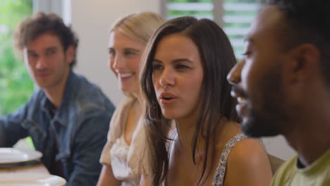 multi-cultural group of friends sitting around table and talking at home dinner party together