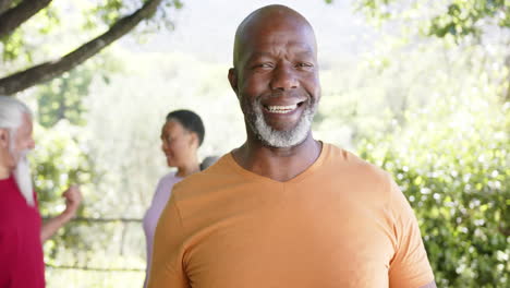 Happy-african-merican-senior-man-holding-yoga-mat,-with-freinds-in-sunny-nature,-slow-motion