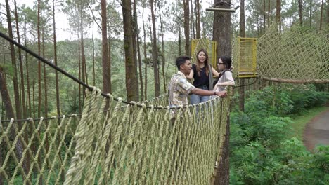 asian young adults chatting on rope bridge in forest adventure