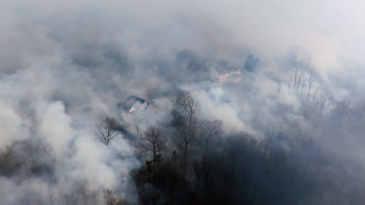 Slow motion aerial drone footage flying towards houses on a ridge that are covered in smoke from a nearby forest fire.