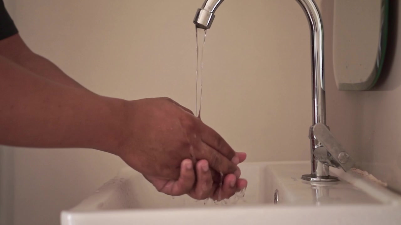 Person turning on a faucet and washing hands in a sink. Clean water, hygiene routine, hand washing, and daily sanitation concept.