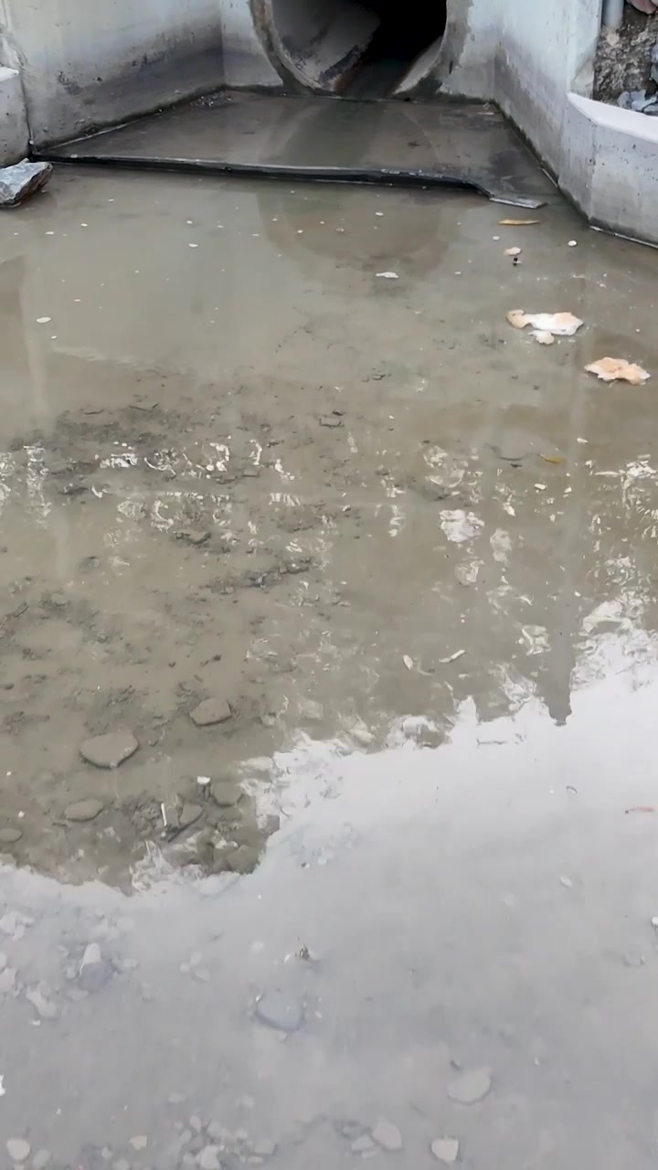 Vertikale Nahaufnahme von trübem Regenwasser, das durch einen Beton-Durchlass in einen Kanal strömt.