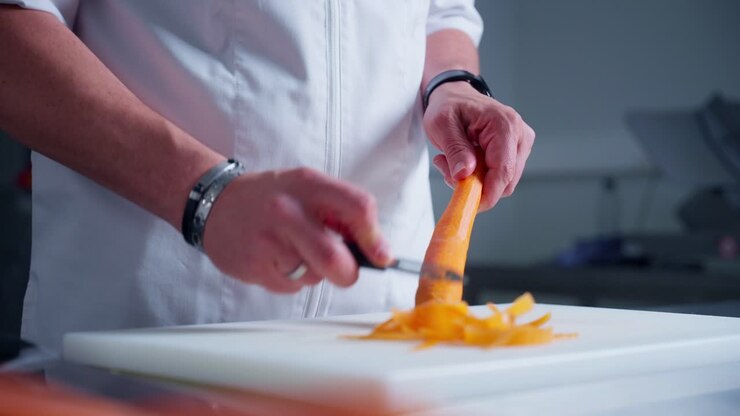 il cuoco sta sbucciando una carota in cucina con un coltello