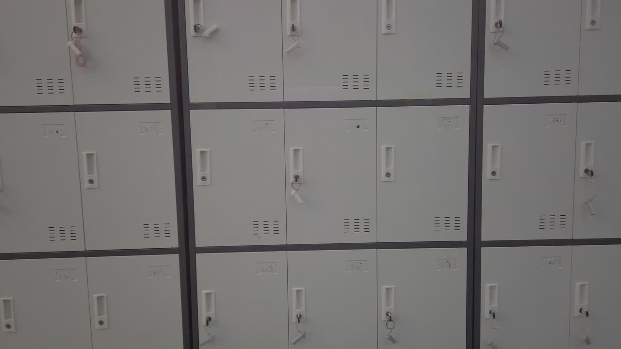 Pan right showing locked storage lockers with keys in indoor corridor, flat lighting