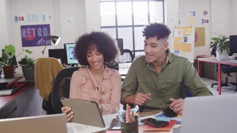 Two-happy-diverse-creative-designers-in-discussion-at-tablet-in-casual-office,-slow-motion