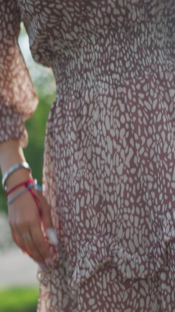 dama en vestido vintage marrón se encuentra con gracia con la mano en la cadera, posando contra el fondo de vegetación exuberante y la luz del sol, su traje complementa la belleza de la naturaleza mientras disfruta al aire libre en zapatillas de deporte casuales