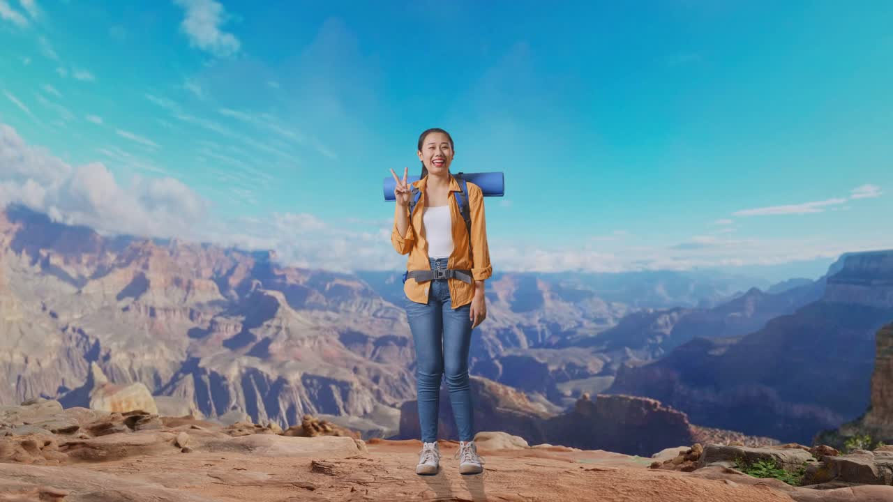 Full Body Of Asian Female Hiker With Mountaineering Backpack Smiling And Showing Peace Gesture While Traveling At The Top Of Mountain