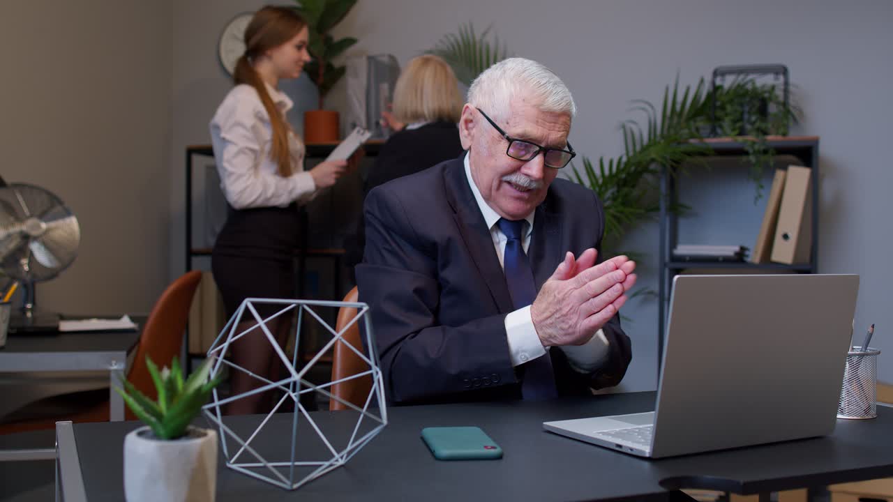 Astuto uomo d'affari anziano che si sfrega le mani, con in mente un piano malizioso e ingannevole, all'interno di un ufficio.