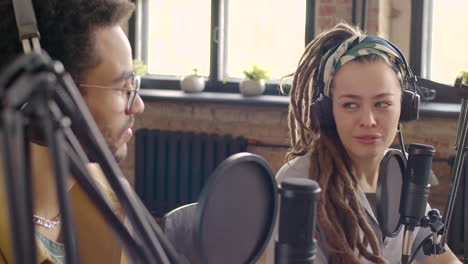 close up view of young man and woman wearing headphones sitting at a table with microphones while they recording a podcast