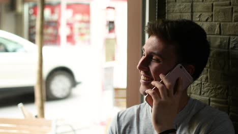 cheerful young man speaking on smartphone near cafe window