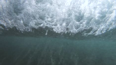 Vista-Submarina-En-Cámara-Lenta-Extrema-De-Una-Ola-Rompiente-En-La-Costa-Tomada-Desde-Debajo-De-La-Ola