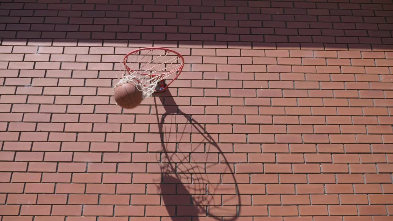 perspectiva frontal de la pelota de baloncesto dando vueltas alrededor del anillo de metal y entra en el aro para el gol en el fondo de la pared de ladrillo rojo