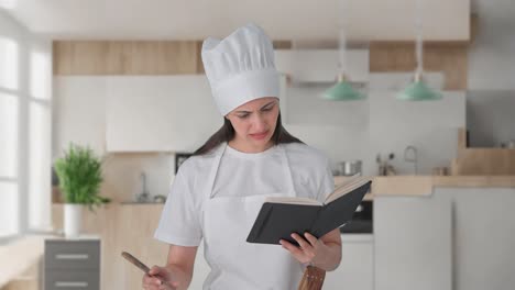confundida mujer india chef profesional haciendo comida a partir de un libro de recetas