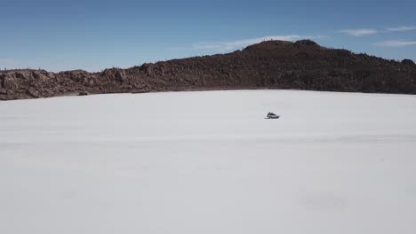 tracking shot of a vehicle driving past an island in the middle of the bolivian salt flats