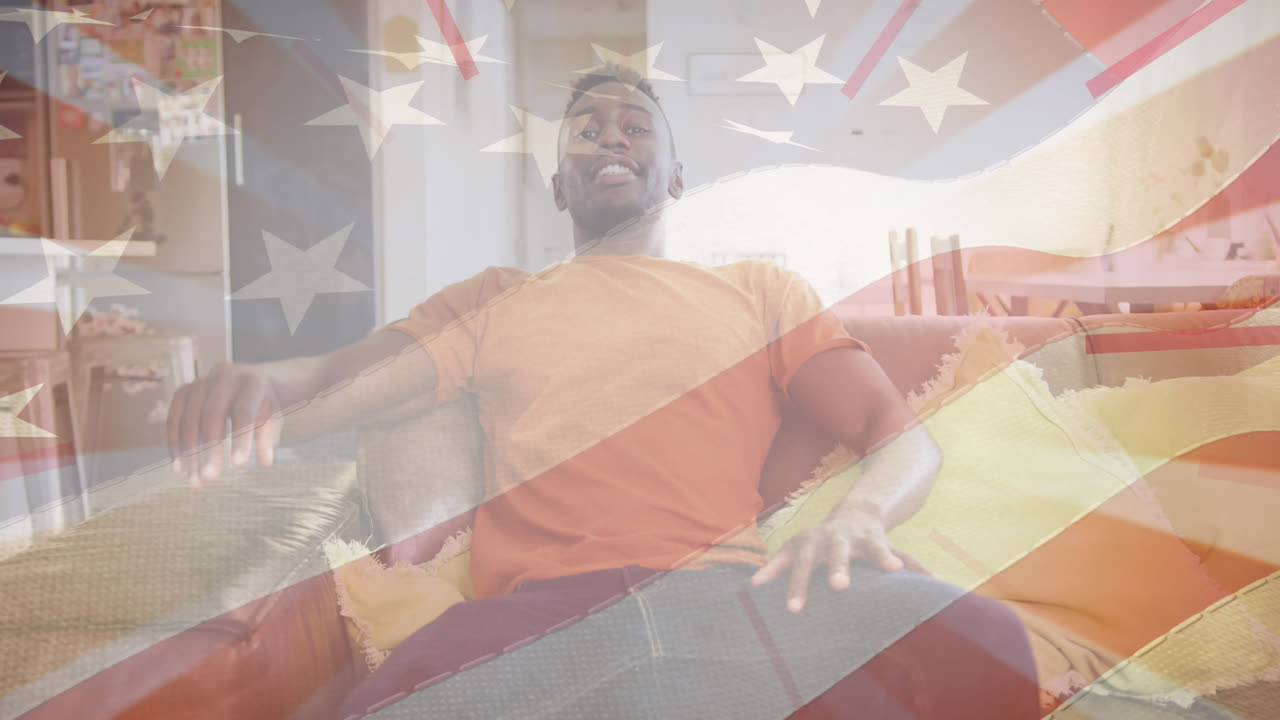 animación de la bandera de los estados unidos de américa sobre un feliz hombre afroamericano sentado en el sofá