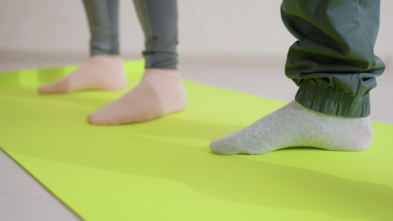 Side leg view of people exercising on bright green fitness mat indoors, showing socks and lower body in close up angle, workout training focus on movement