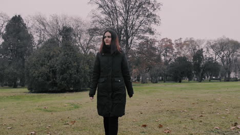 a lonely woman walking in the park, fallowing shot, on a greenfield ascending above