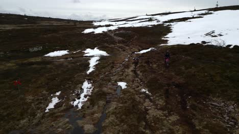 a woman and her frenchie walking on a mountain path by the snow line