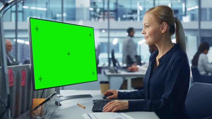 Ufficio moderno e diversificato: donna d'affari sicura di sé che usa un computer desktop con display mock-up green screen. Manager che lavora al supporto clienti e-commerce, marketing di progetto