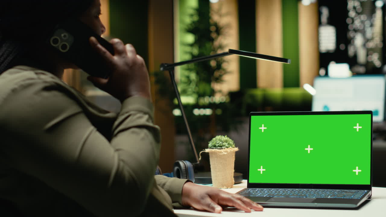 Isolated green screen on laptop next to black woman answering a phone call