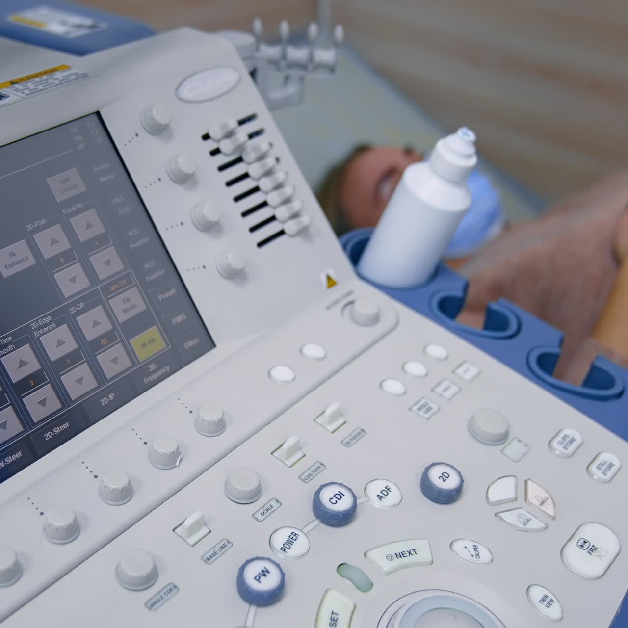 Touch screen and keyboard of ultrasound machine. Male medic applies ultrasonic device to a patient's belly. High angle view
