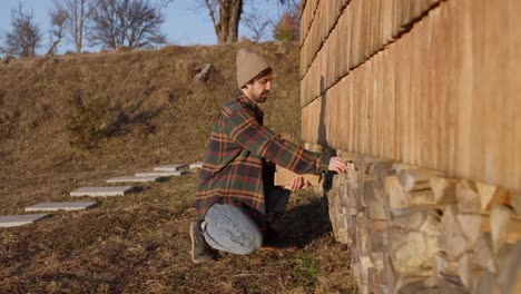 man stacking firewood by a cabin
