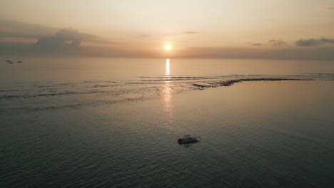 Barco-A-La-Deriva-Durante-El-Amanecer-De-Bali,-Antena-Cinematográfica,-El-Sol-Sale-En-El-Horizonte-De-Un-Mar-En-Calma