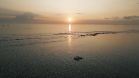 barco a la deriva durante el amanecer de bali, antena cinematográfica, el sol se está levantando en el horizonte de un mar tranquilo