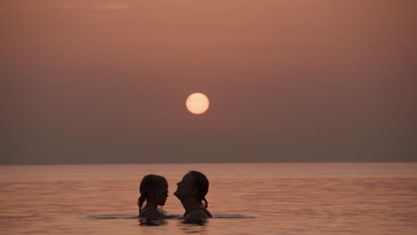 mother and daughter playing in the ocean at sunset