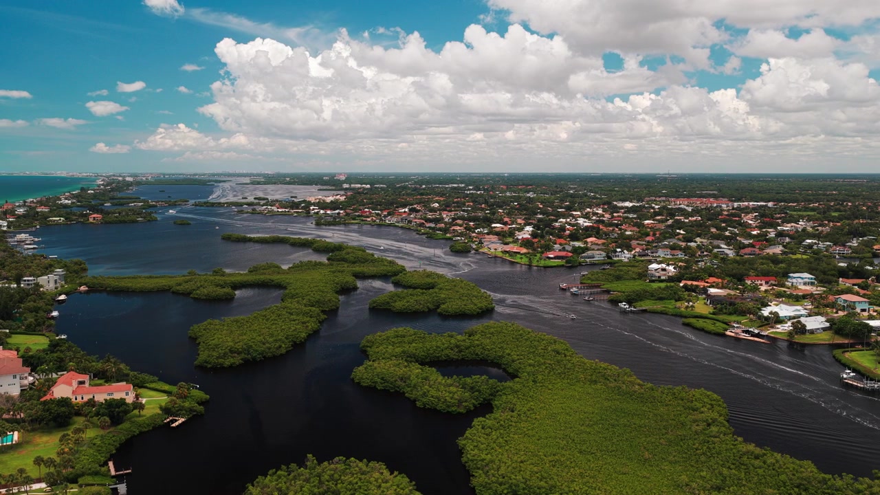 Kabarık yaz bulutları altında yeşil mangrov adaları ile alçak katlı bir Florida mahallesi arasında kıvrılan karanlık kıyı içi kanal