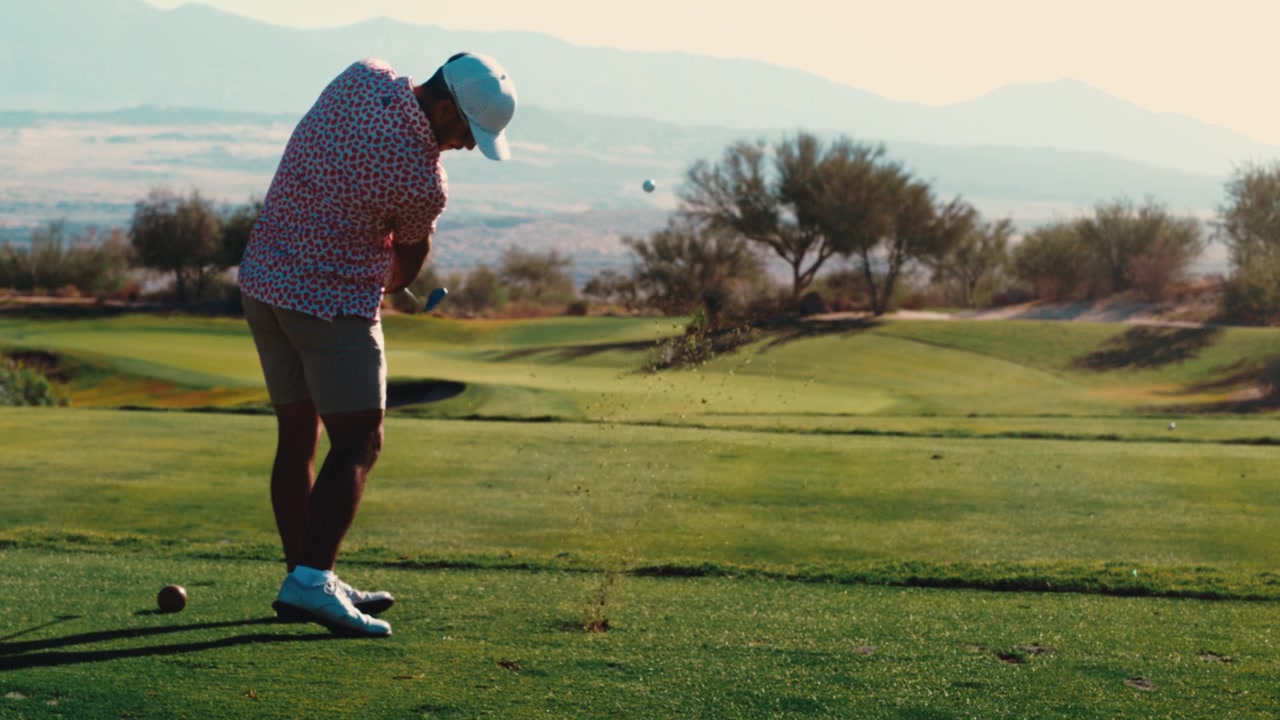 A golfer compresses an iron shot on par 3 and sends divot spray flying in warm golden light on a desert course, captured in slow motion. Strong for premium golf promos.